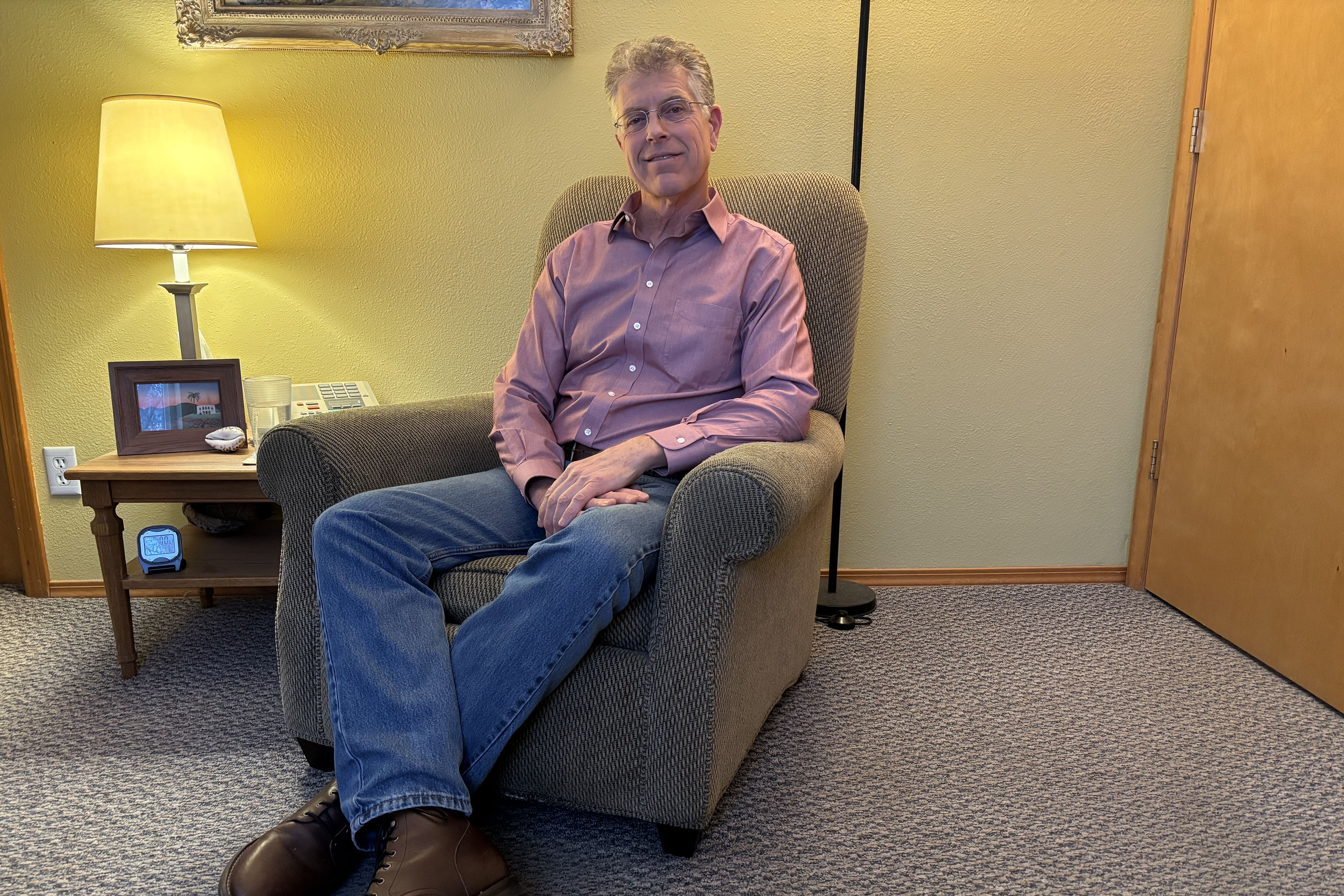 A man sits in a chair and faces the camera.